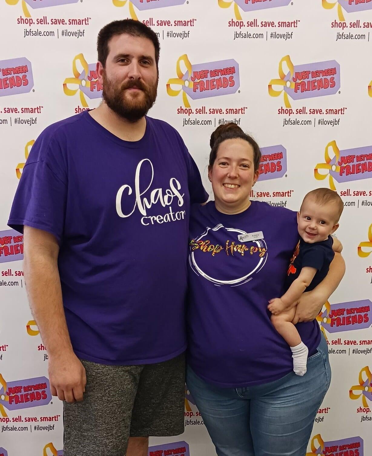 JBF Poconos owners, Kyle and Ashley Elmer, standing together with baby Owen in front of a JBF banner.