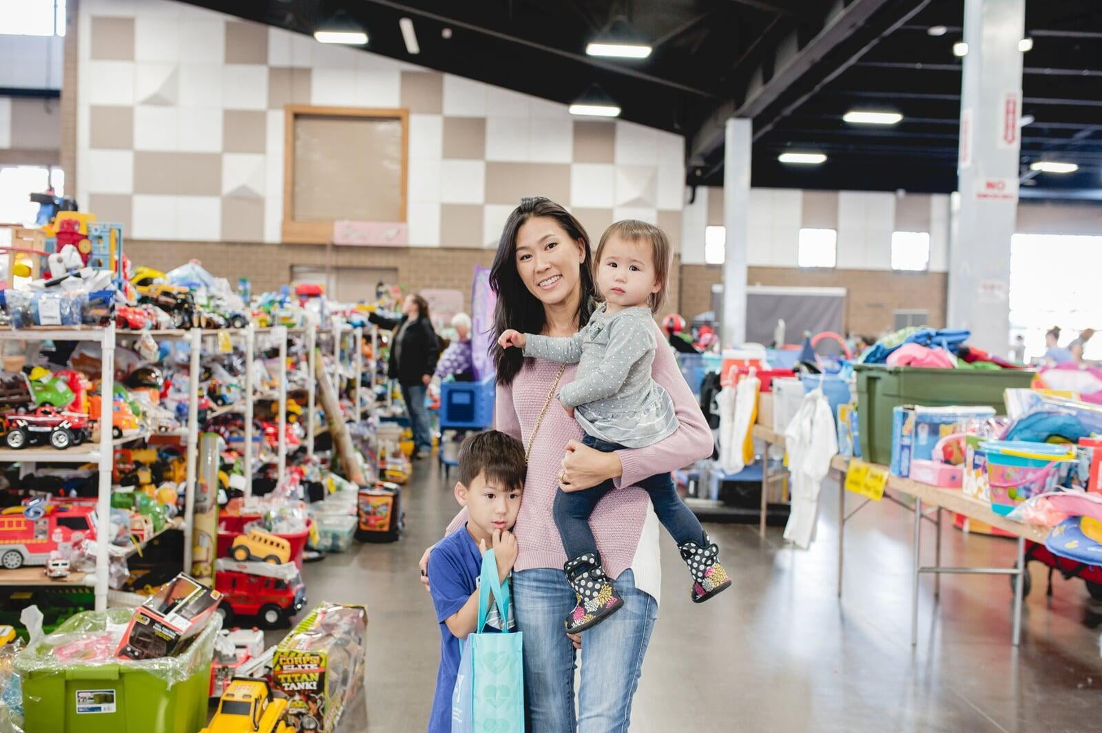 Mom holds daughter and son standing next to her while she shops the local JBF sale.